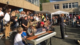 Eine Lehrerein dirigiert eine Schüler-Bigband auf dem Schulhof.  