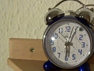 Ein Wecker auf einem Nachttisch zeigt kurz nach sechs Uhr an.  